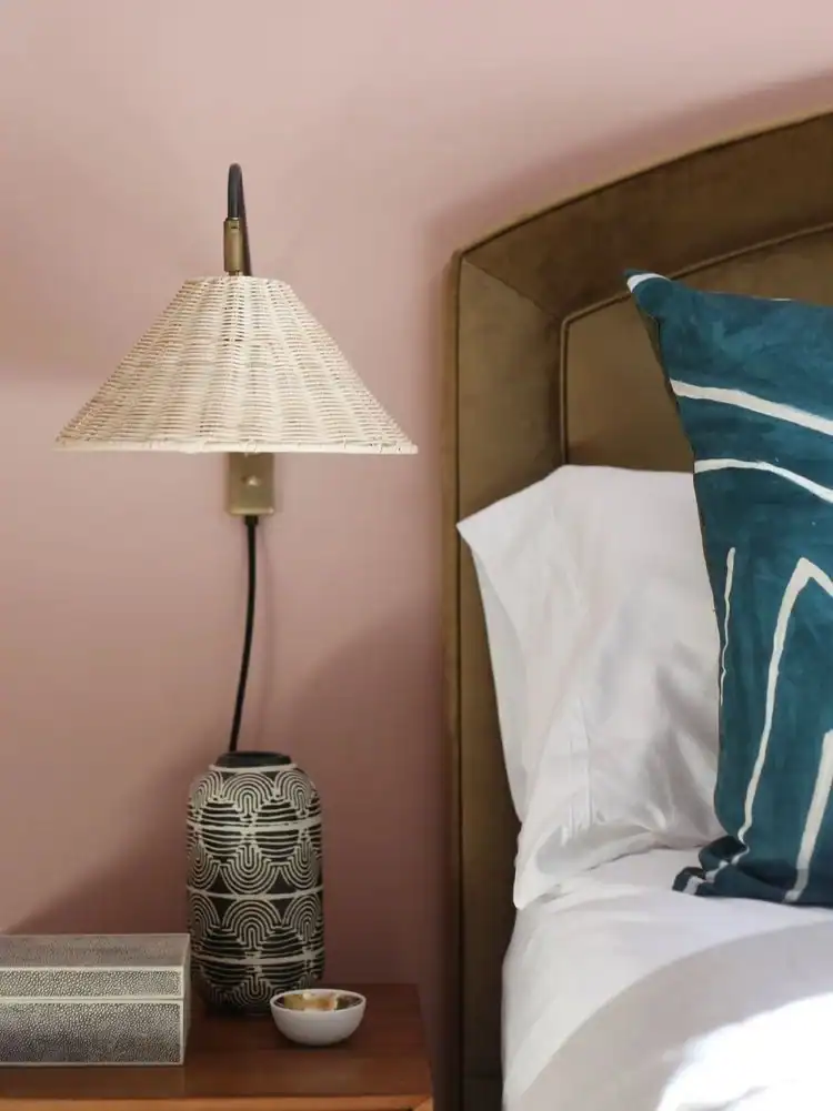 Close up of a bedside with a rattan sconce light. Calm Bedroom Ideas
