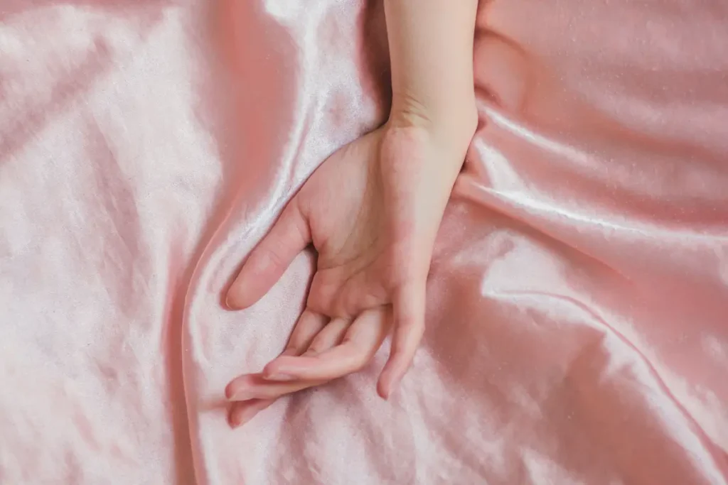 A close-up of a female hand resting gently on an elegant pink silk sheet, evoking serenity and comfort.