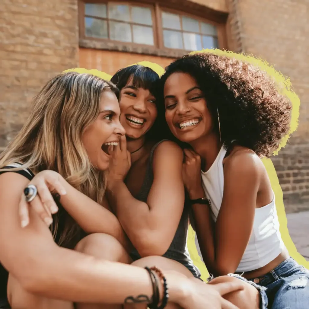 Three-young-female-friends-laughing-while-sitting-down-outside-a-building