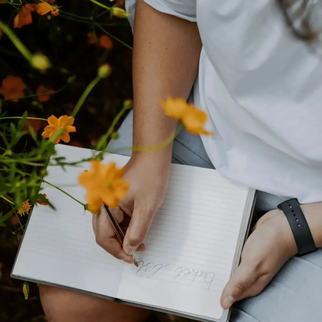 Woman writing in notebook around flowers