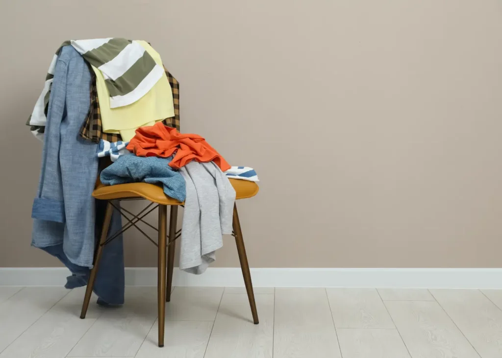 Different clothes on chair near light grey wall, space for text. Daily Cleaning Habits