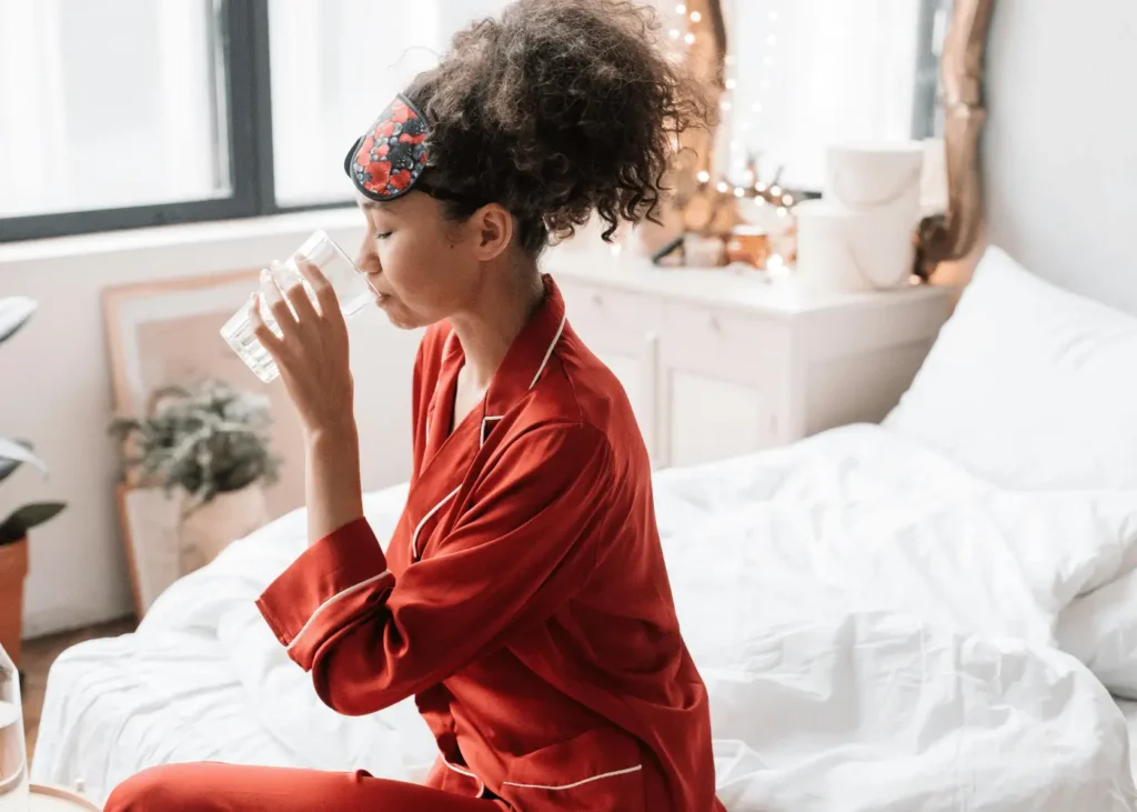 Woman Drinking Water on her bed in her pyjamas. How To Deep Clean Your Room