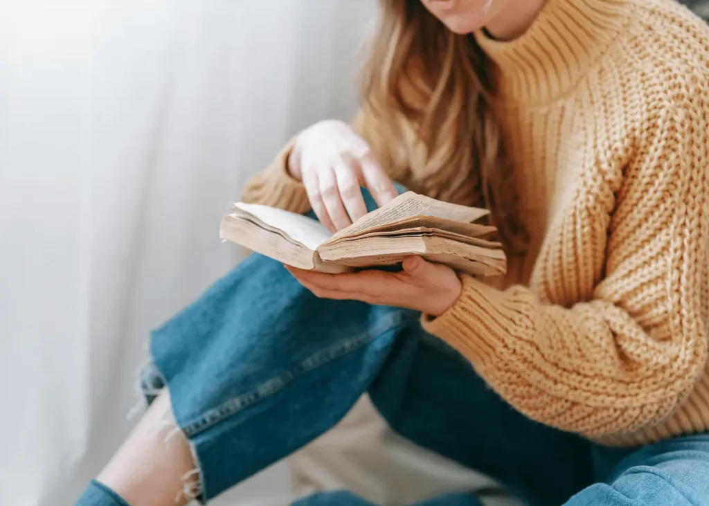 woman wearing a chunky knit sweater reading a book. self-care sunday ideas