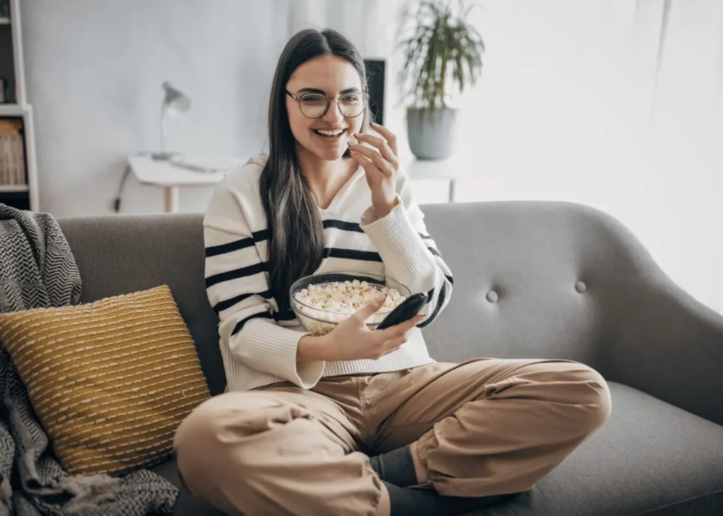 young woman on a sofa eating popcorn, watching a movie. Rainy day activities