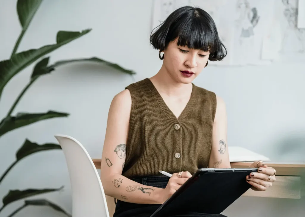 Asian female artist sitting on white chair and using tablet. this post is about how to create a hobby menu