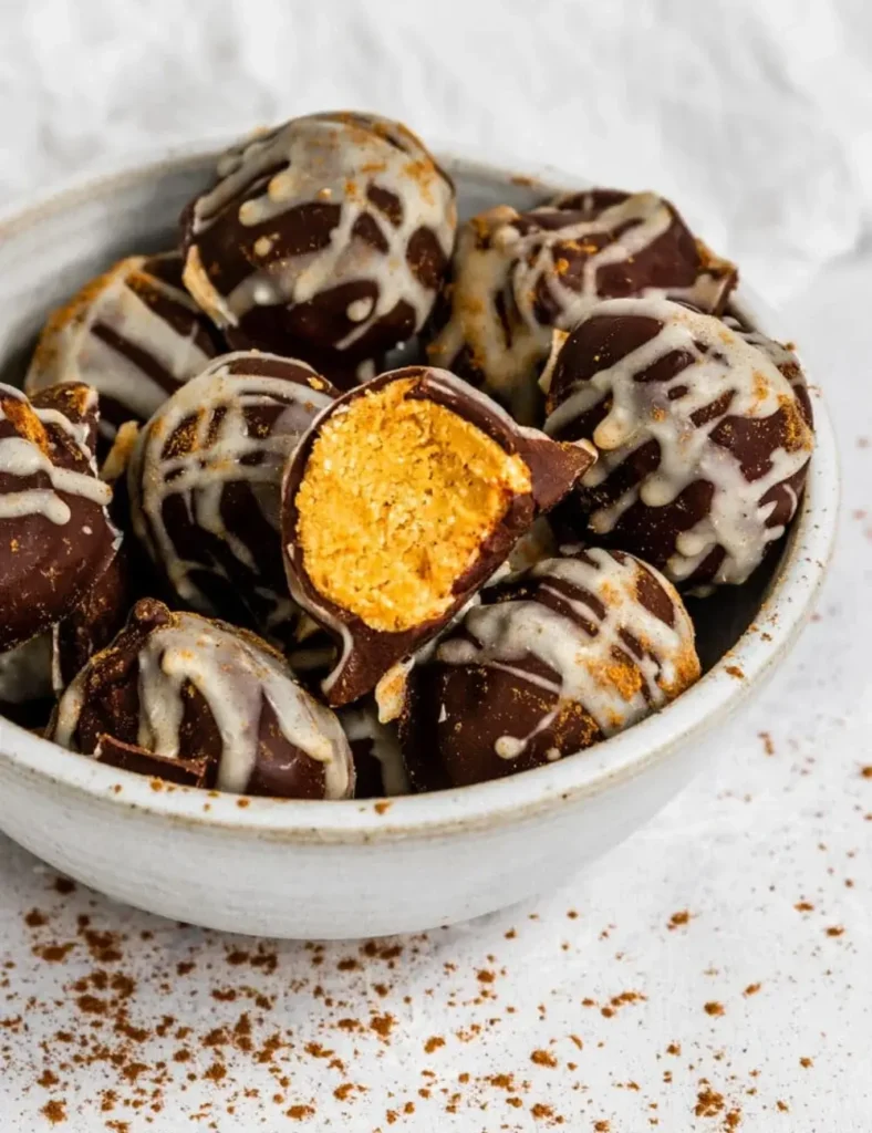 Chocolate-covered pumpkin pie truffles in a bowl with one bitten to show the filling