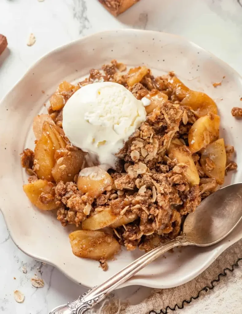 Vegan apple crisp in a baking dish with a golden oat topping and a scoop of vanilla ice cream