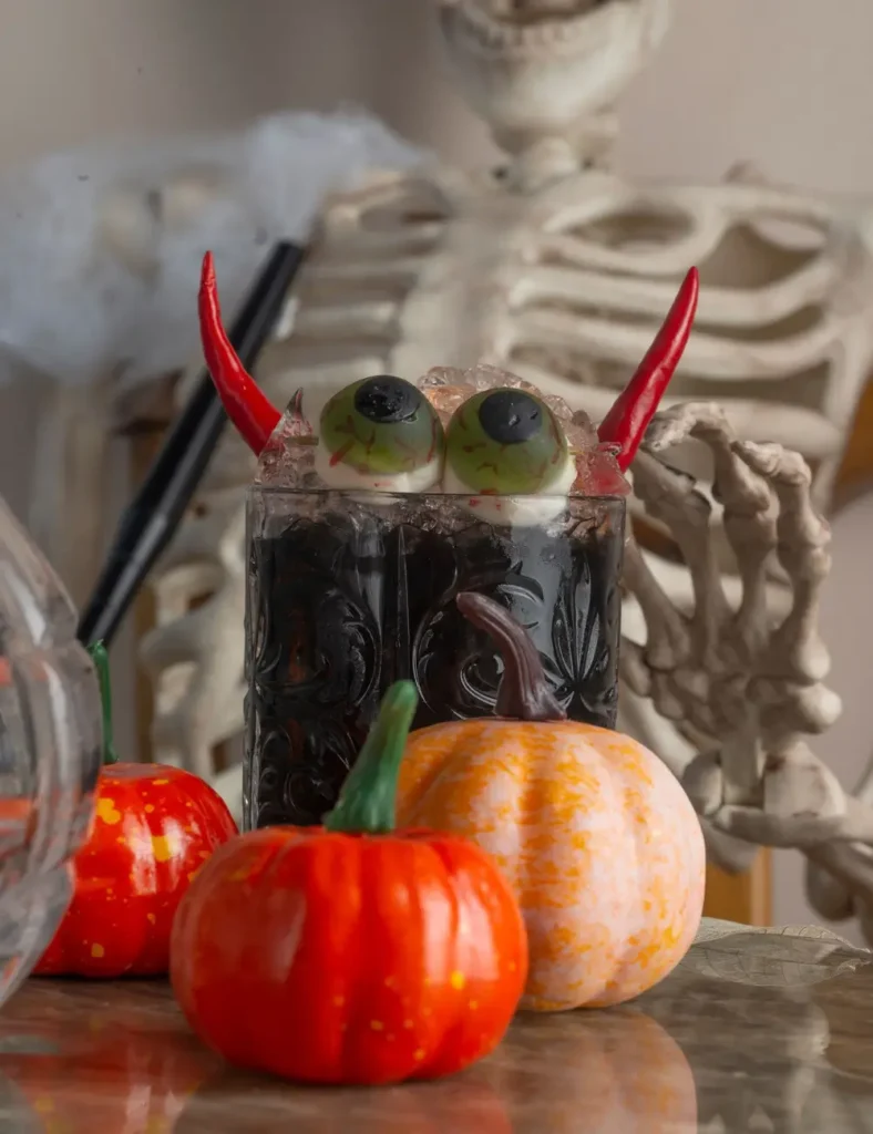 A creepy Halloween cocktail with eyeballs and pumpkins in front of a skeleton decoration.
