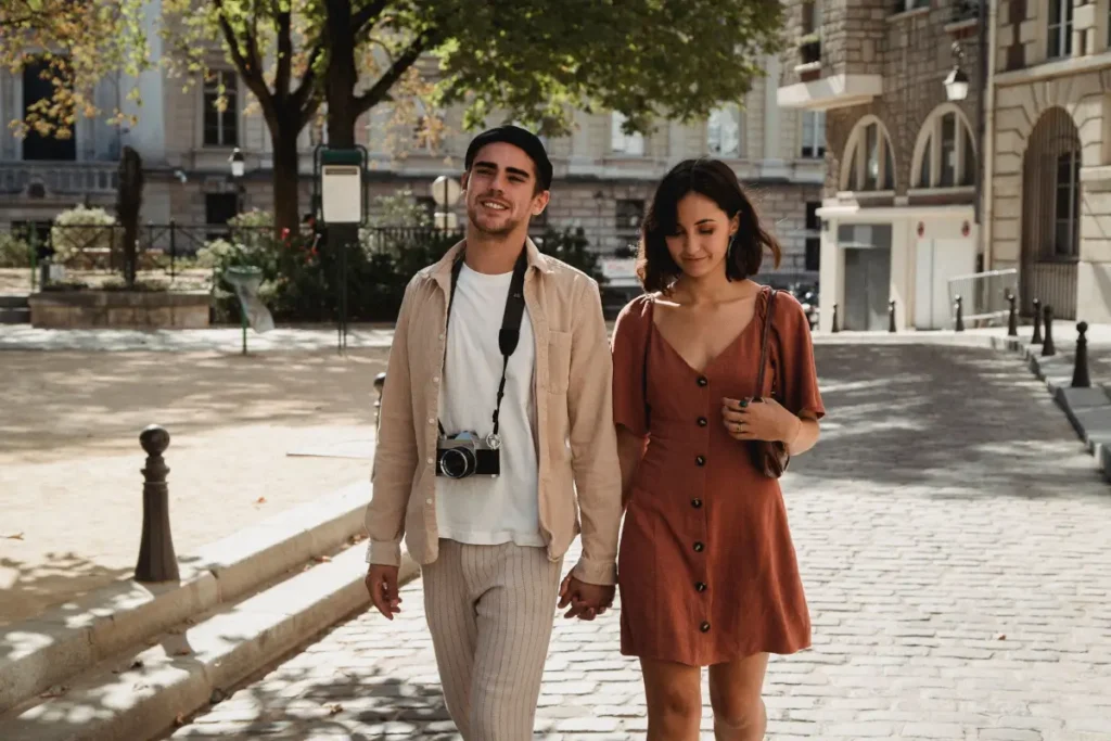 A stylish couple walks hand in hand on a sunny cobblestone street, exuding romance and fashion. Couples Bucket List Ideas