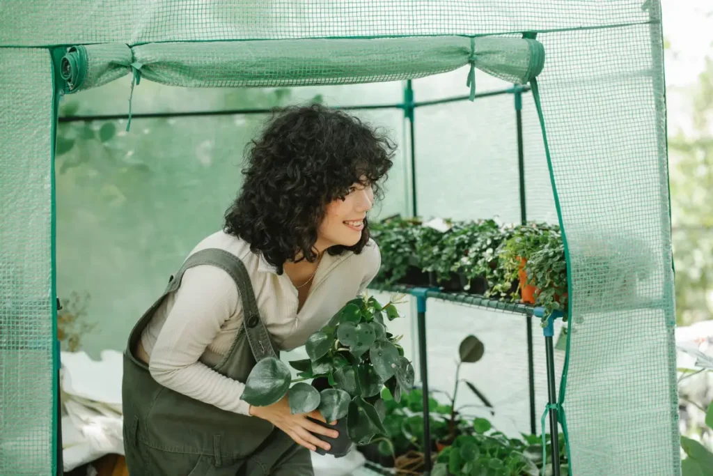 Smiling woman with curly hair caring for plants in a greenhouse garden. Hobbies For Women In Their 20s