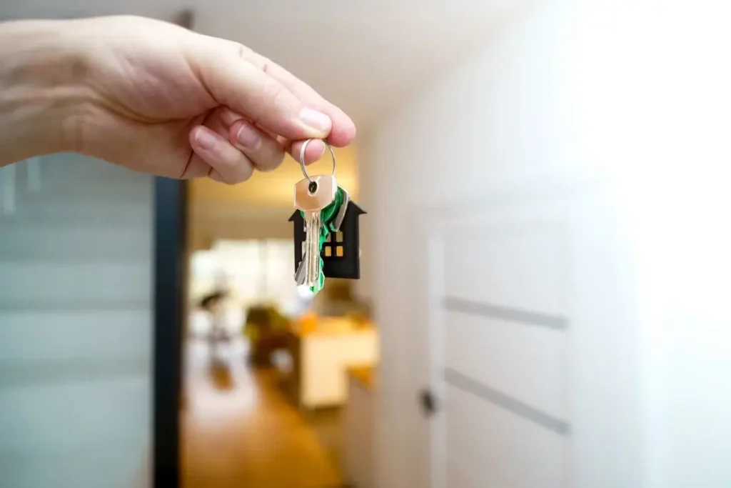 A hand holding house keys inside a modern apartment, symbolizing new property ownership or rental. Funny House Names
