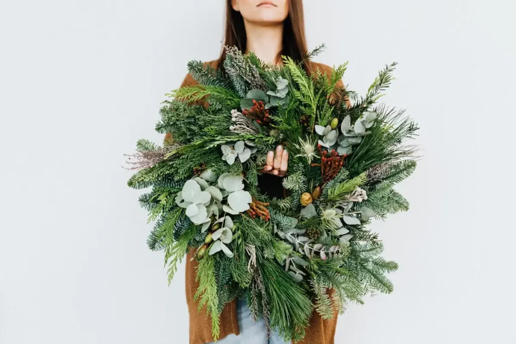 A lush Christmas wreath being held by a woman against a white background. Hobbies for Women Over 40
