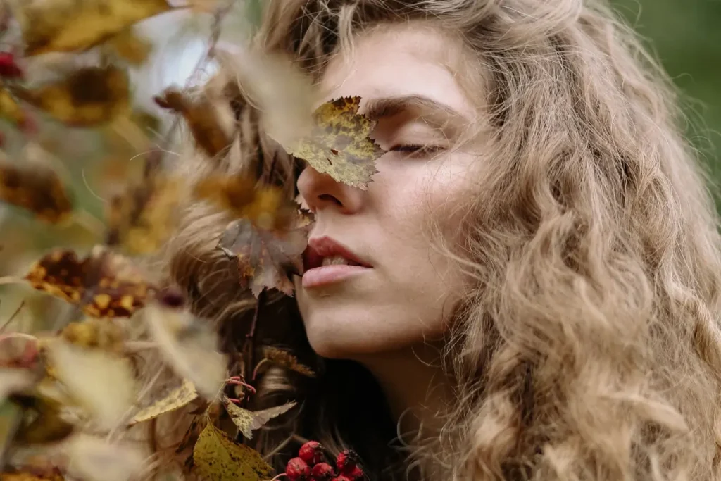 A serene portrait of a woman with curly hair embracing autumn foliage, exuding natural beauty. Fall Journal Prompts