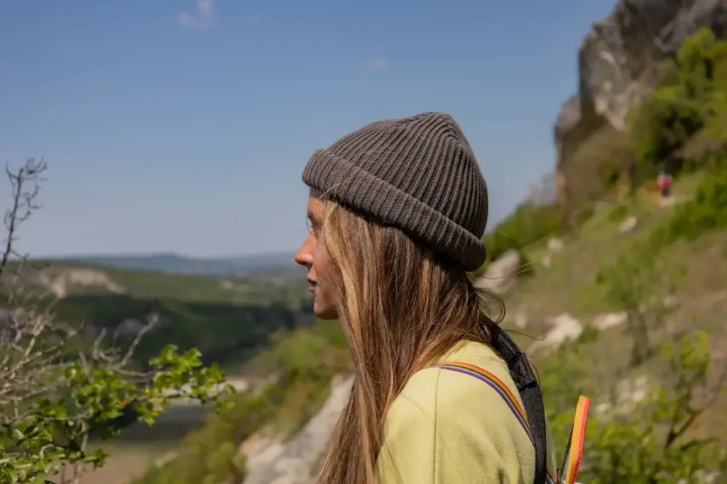 A woman wearing a hat enjoys the scenic mountain landscape during a sunny hike. Hobbies for Women Over 40