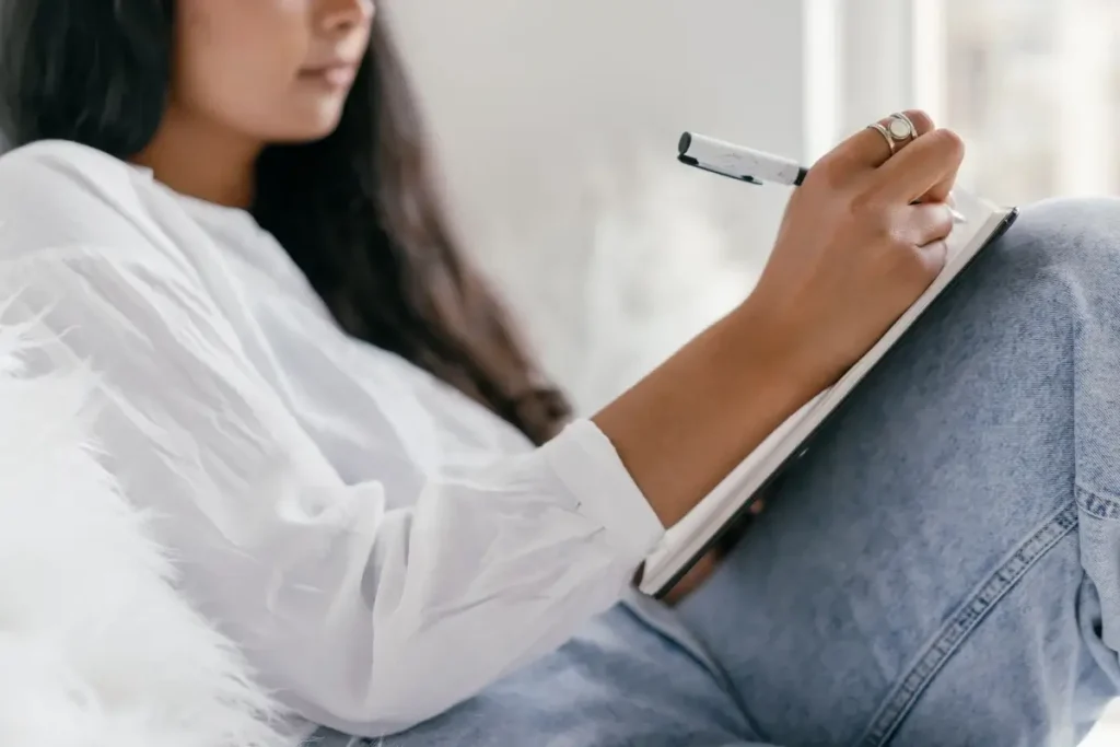 Close-up of a woman writing in a notebook, showcasing creativity and focus. Self-Care Bingo