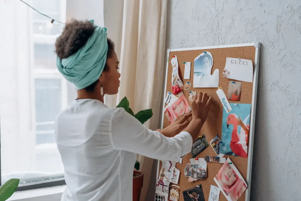 Woman with afro hair organizing a vision board indoors, focusing on creativity and planning. 
