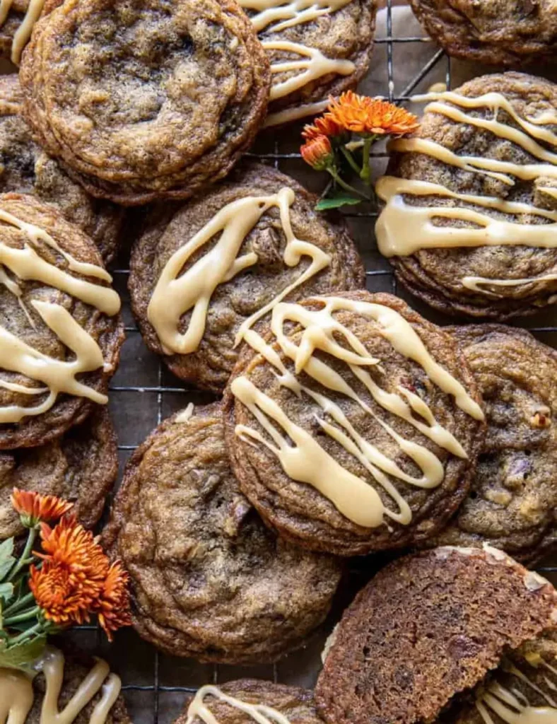 Stack of chewy brown sugar cookies drizzled with maple glaze, garnished with orange mums on a wire cooling rack.