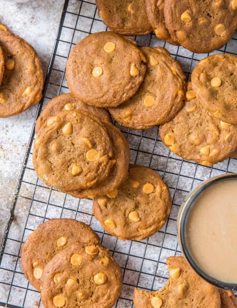 Overhead shot of gingerbread cookies studded with butterscotch chips, cooling on a wire rack next to a mug of coffee.