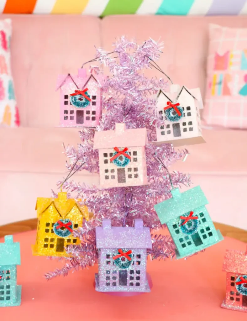 Mini paper mache house ornaments spray-painted in bright colors and coated in iridescent glitter, with tiny wreaths on the doors.