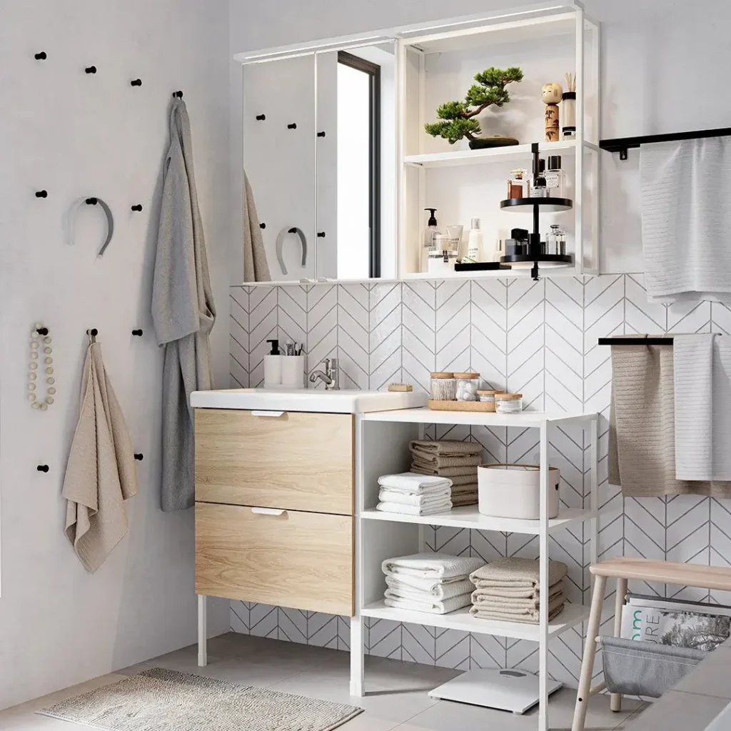 Scandinavian bathroom with oak vanity, white chevron tile, open shelving stacked with folded towels, and a wall pegboard with hooks