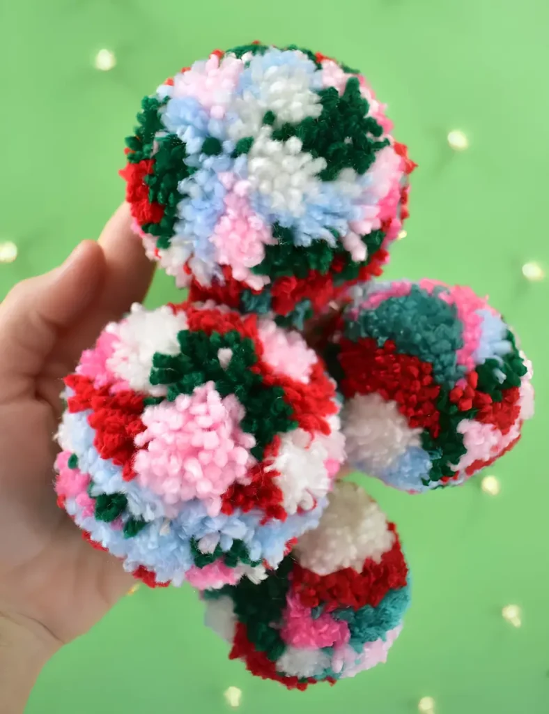 Dense multicolored yarn pom pom ornaments in pink, red and green hanging on a tree.