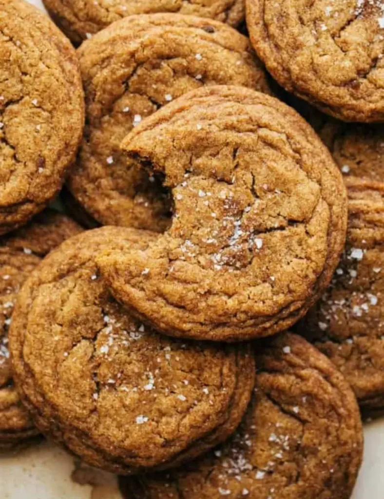 Close-up of chewy pumpkin cookies topped with flaky sea salt, one broken in half to show the soft center.