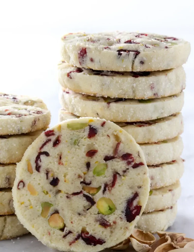Stack of round icebox cookies with a sugared edge, showing cross sections studded with dried cranberries and chopped pistachios.