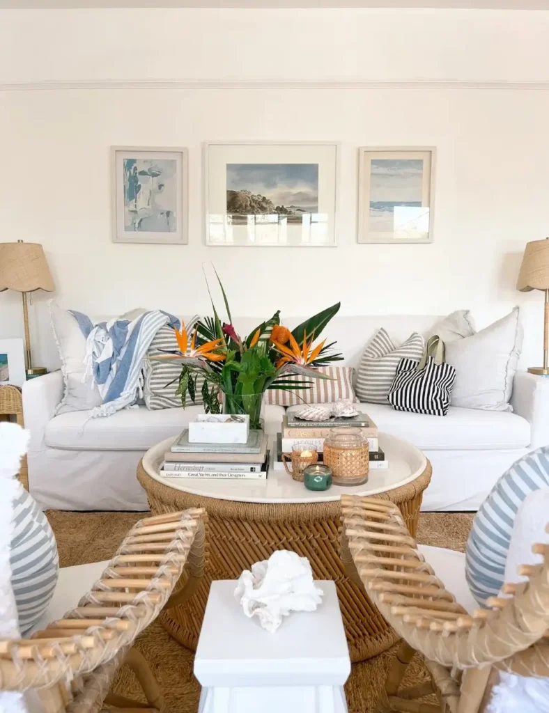 Coastal living room with white slipcovered sofa, rattan chairs, and a large vase of bird of paradise flowers on a woven coffee table.