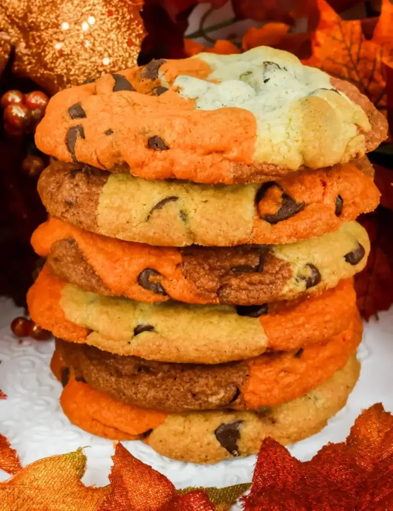 Stack of chocolate chip cookies marbled with orange and white dough, styled with fall leaf decorations in the background.