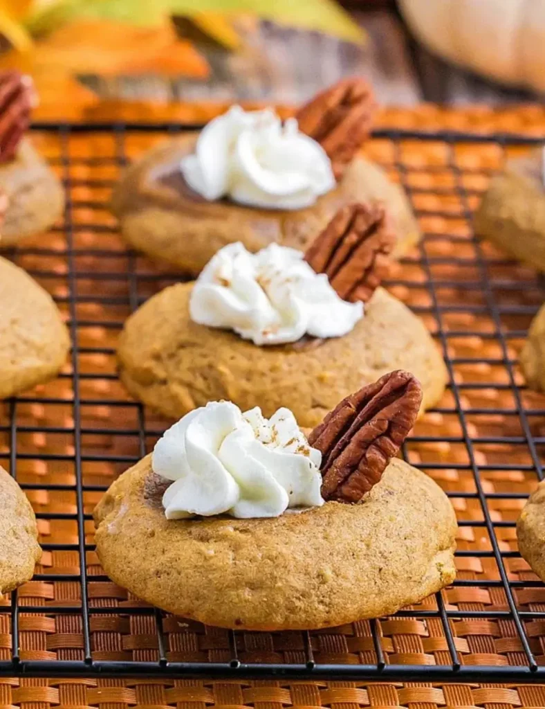 Soft pumpkin cookies topped with whipped cream and a pecan half, styled like mini pumpkin pies.