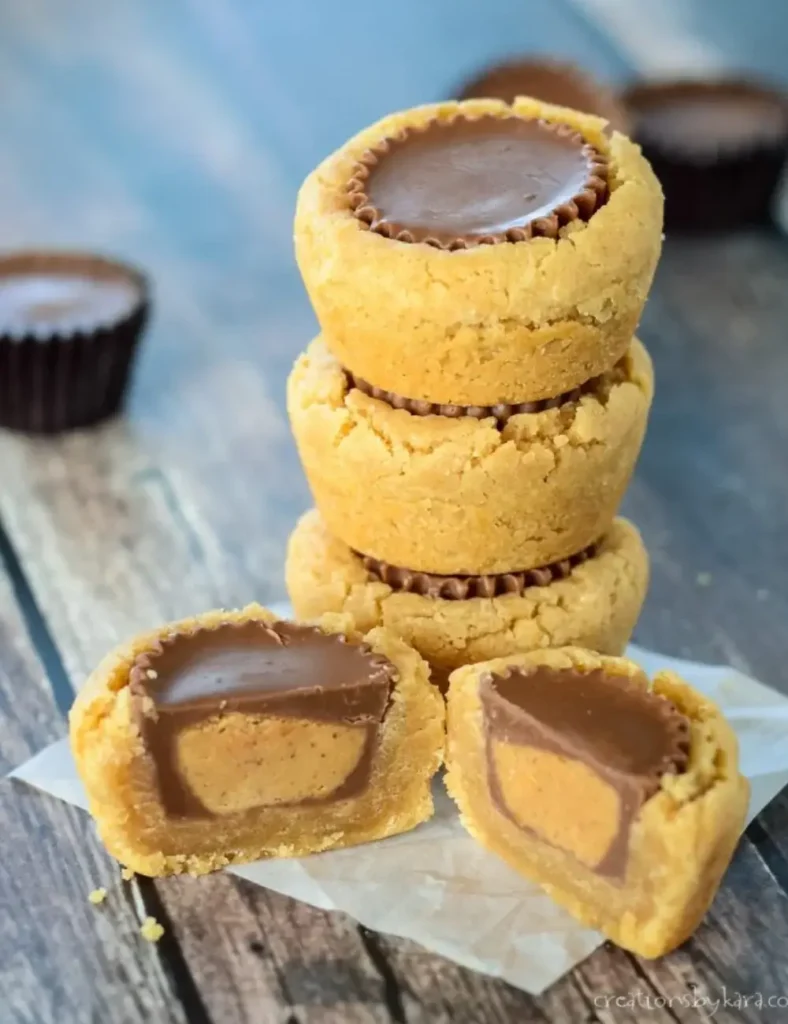 Stack of peanut butter cookies with a whole Reese's cup baked into the center, two halves in front showing the chocolate and peanut butter filling inside.