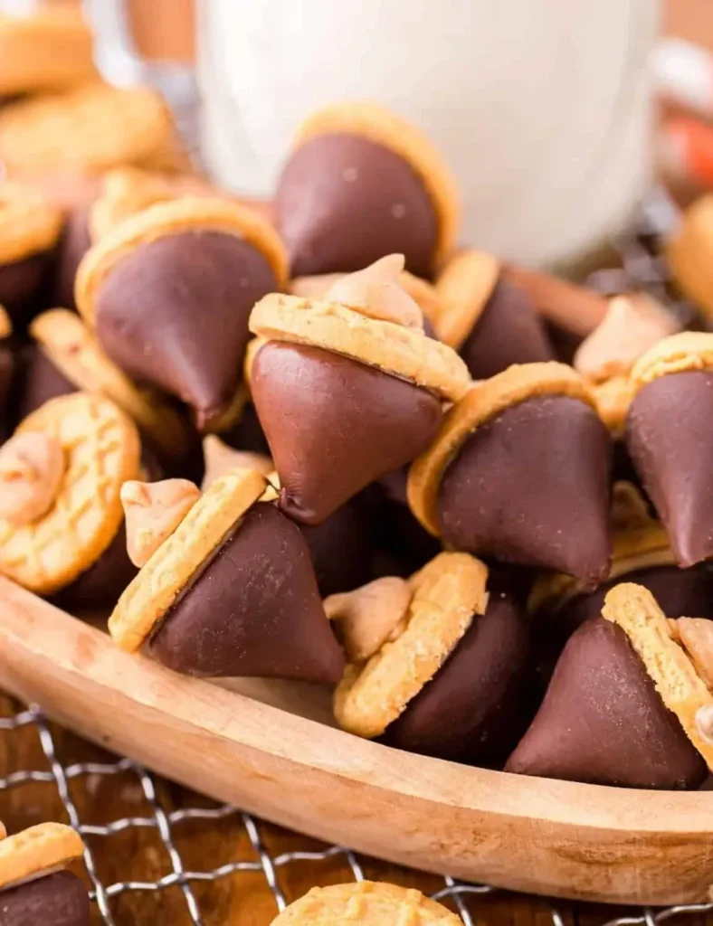 No-bake acorn-shaped treats made from chocolate Hershey's Kisses and Nutter Butter cookies, piled in a wooden bowl.