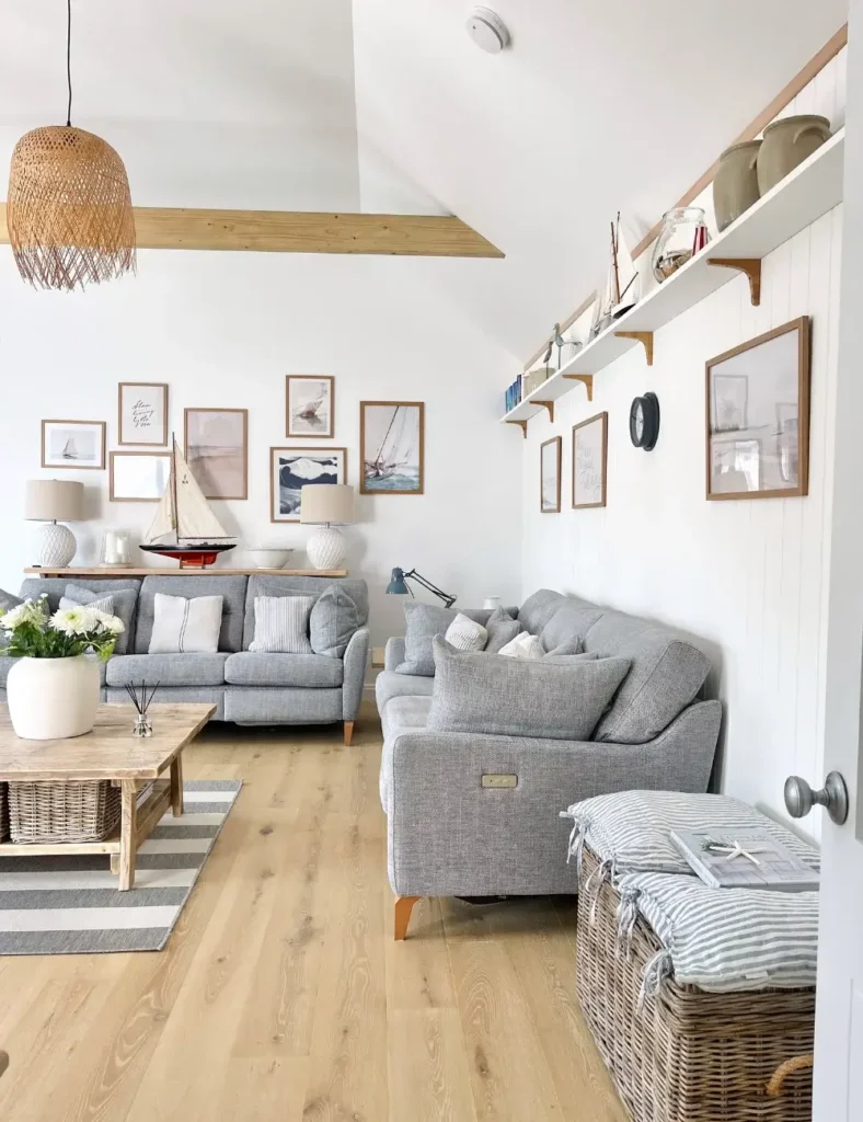 Coastal cottage living room with a sailboat print gallery wall, model sailboat on a console table, and gray sofas on a striped rug.