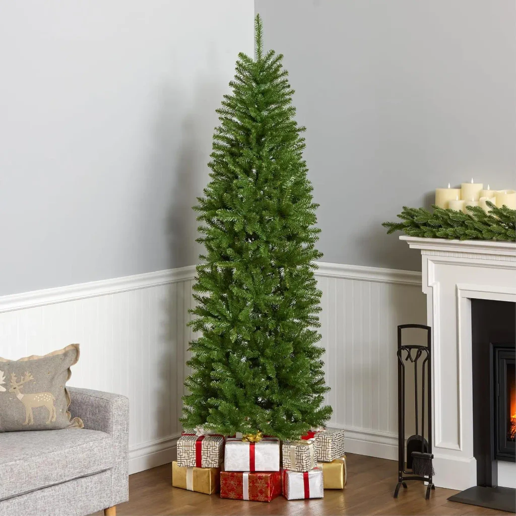Slim pencil Christmas tree standing in a corner of a small living room with wrapped gifts at its base.