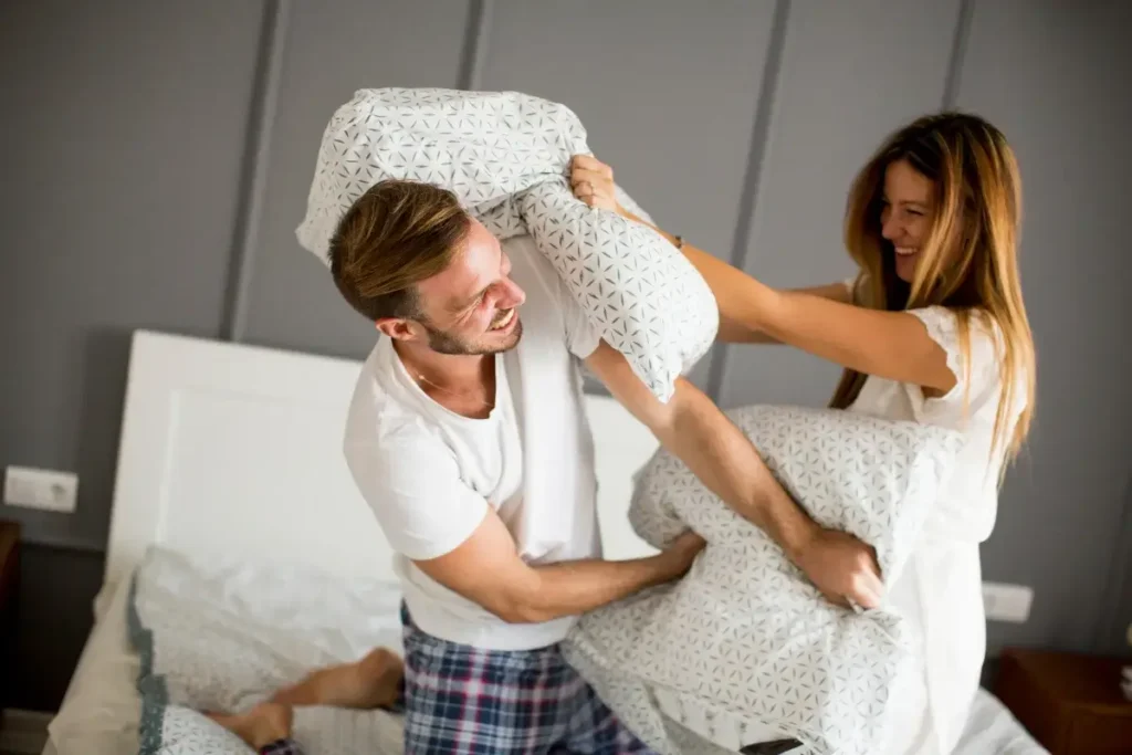 A cheerful moment of a couple having a playful pillow fight indoors. Fun Date Night at Home Ideas