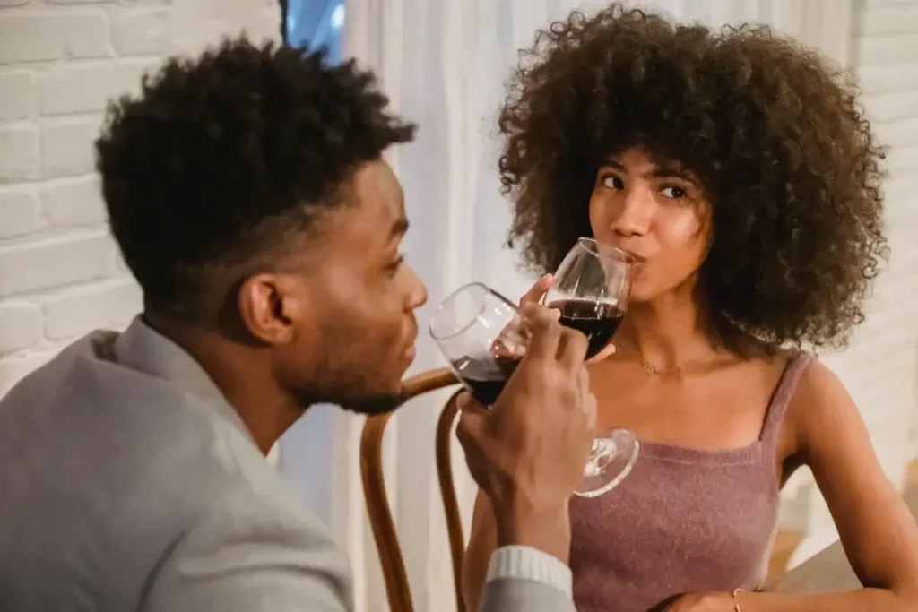A couple enjoying a romantic dinner, toasting with red wine in a cozy setting. Fun Date Night at Home Ideas
