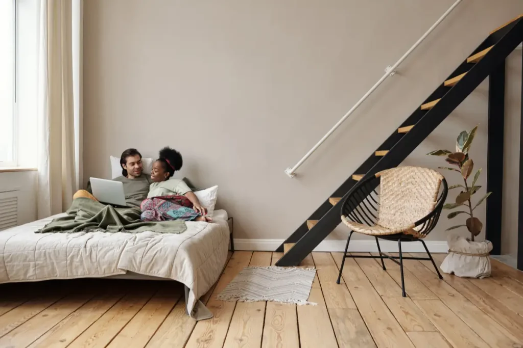 A couple enjoys a relaxing day indoors, embracing on a bed with a laptop in a stylish apartment.