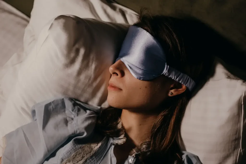 A serene scene of a woman wearing a blue eye mask, sleeping soundly in a cozy indoors setting. self-care ideas for women
