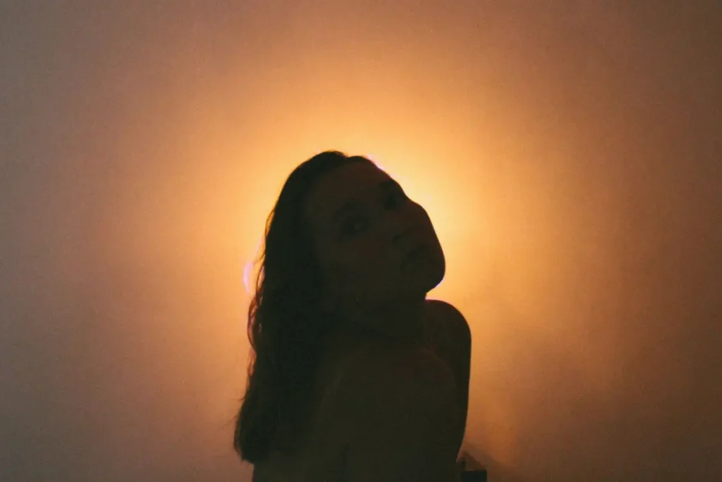 Artistic silhouette of a woman backlit by warm yellow light, creating a dramatic mood.

