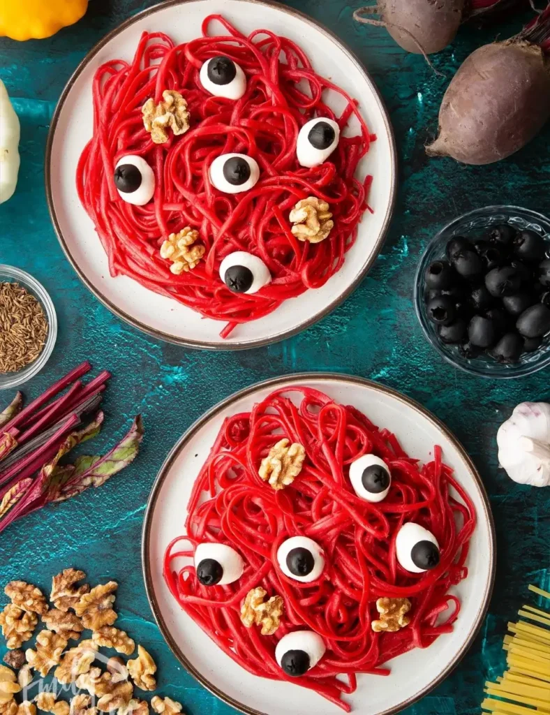 Beetroot-dyed red linguine on a white plate topped with walnut halves and mozzarella eyeballs with olive pupils