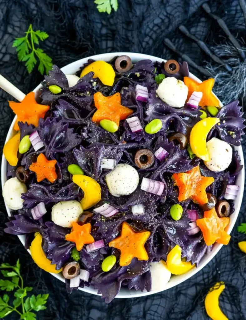 Black farfalle pasta salad with bell peppers cut into stars and moons, edamame, and mozzarella balls in a white bowl