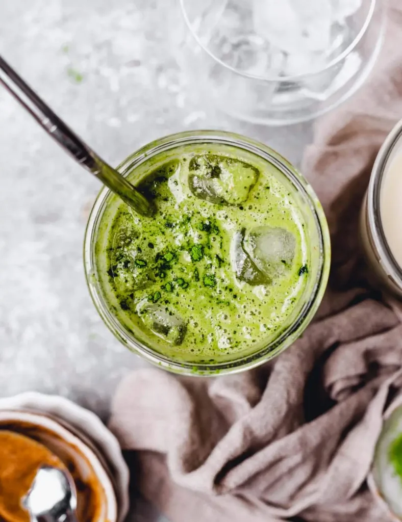 Bright green matcha protein shake in a tall glass over ice with matcha powder dusted on top