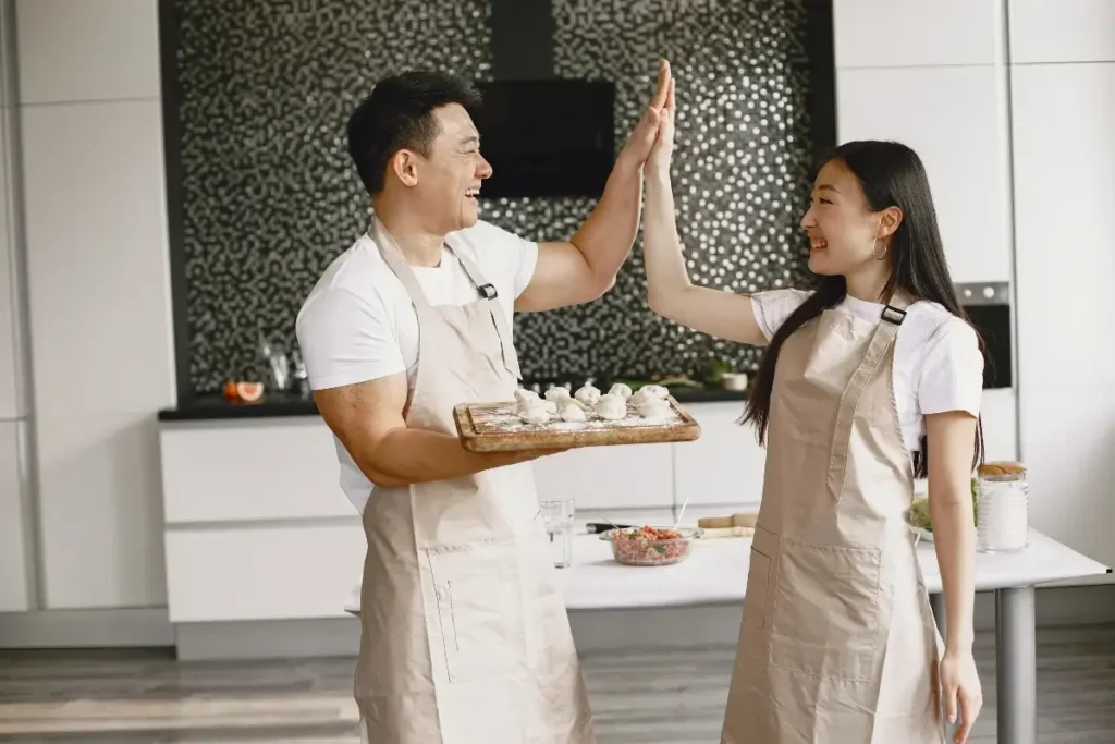 Cheerful couple shares a high-five while making dumplings together in a modern kitchen. Fun Date Night at Home Ideas