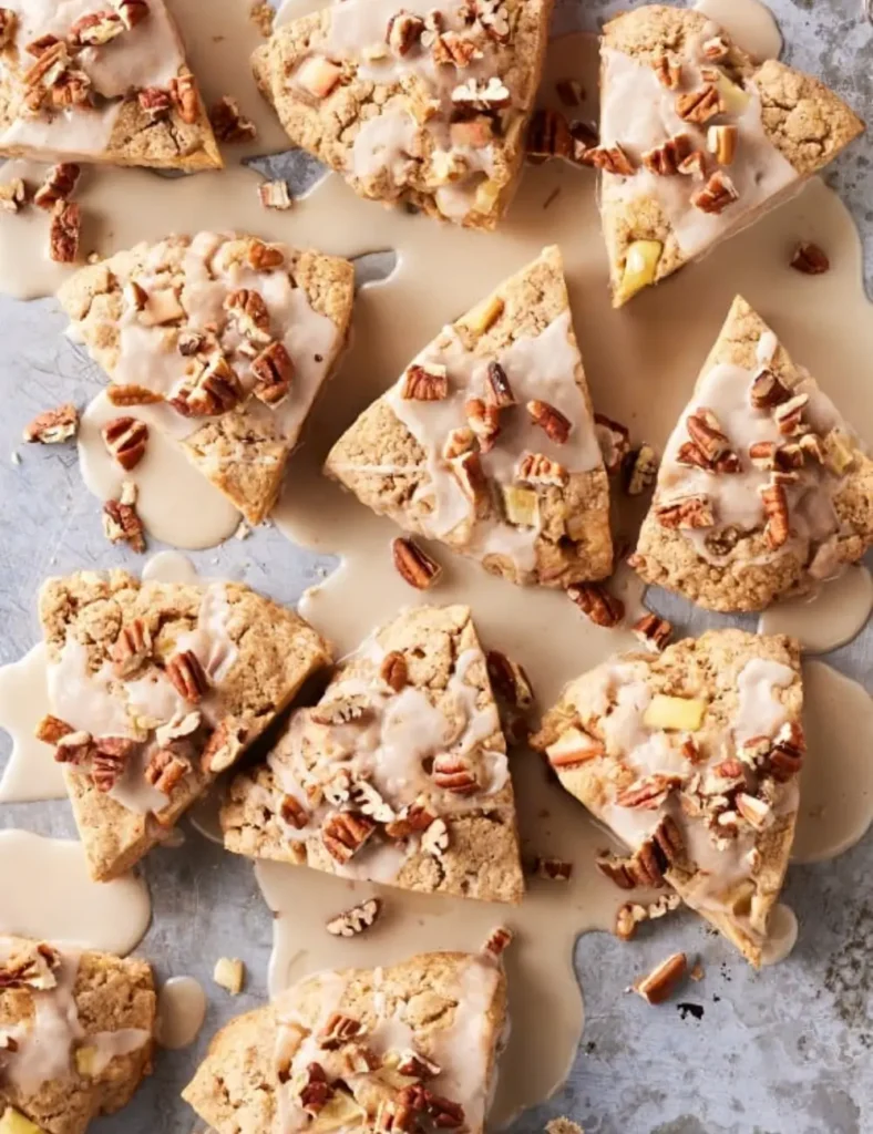Cinnamon apple scones cut into triangles, topped with chopped pecans and a drizzle of glaze