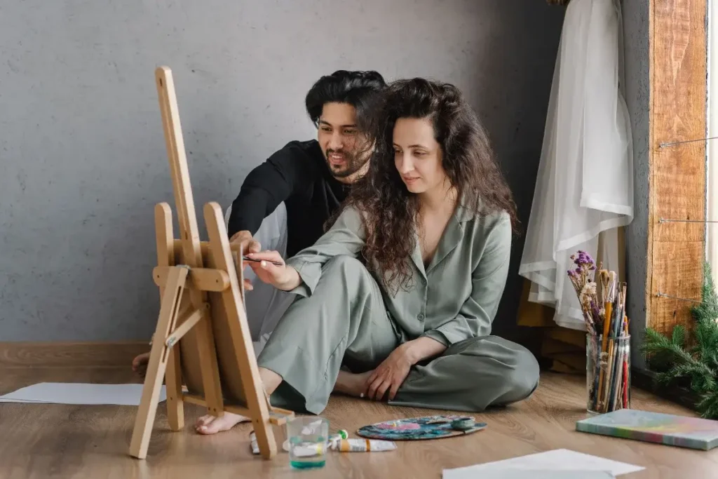 Couple painting at home, showcasing artistic collaboration and creativity in a relaxed setting. Fun Date Night at Home Ideas