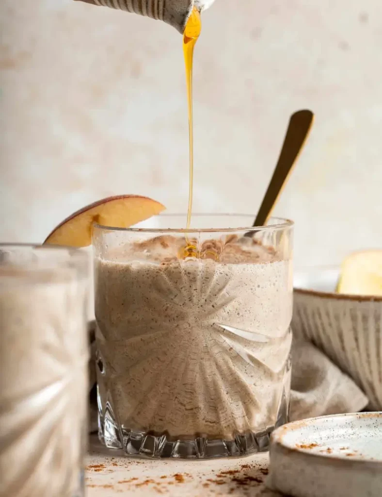 Creamy apple pie smoothie in a glass with sliced apple and cinnamon on the side