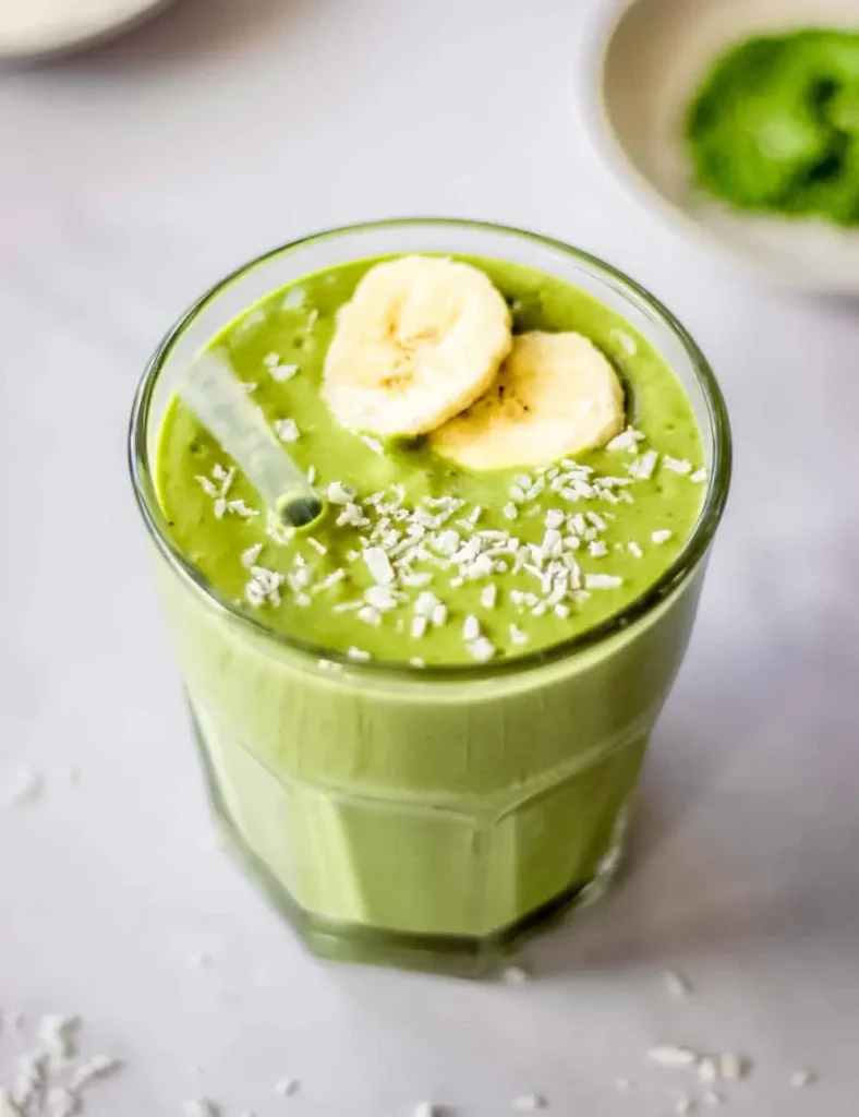 Creamy green banana matcha smoothie in a short glass, topped with banana slices and shredded coconut