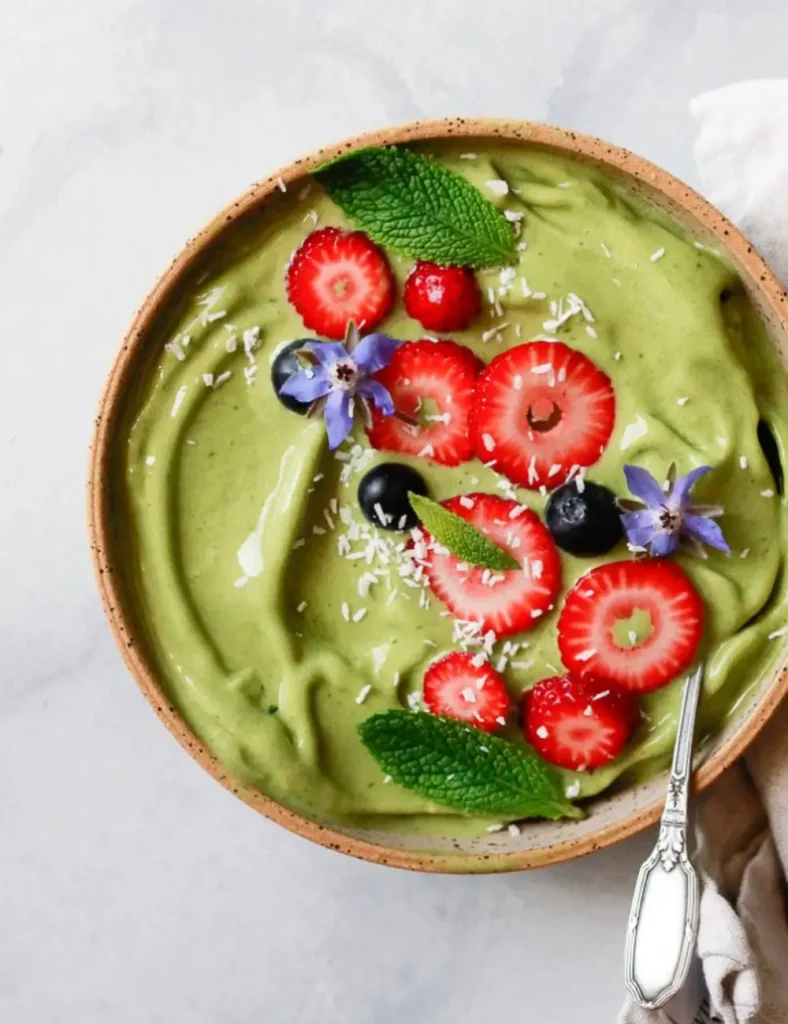 Green matcha smoothie bowl topped with sliced strawberries, blueberries, and fresh mint