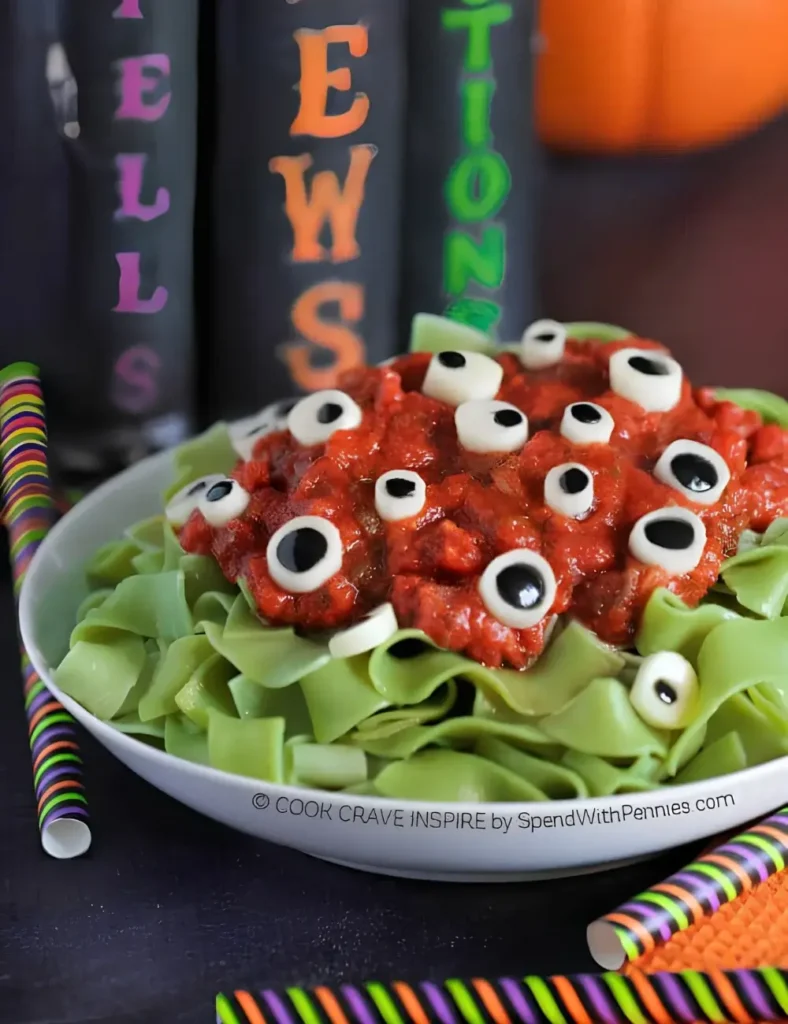 Green spinach pasta with tomato sauce topped with string cheese and black olive eyeballs in a white bowl