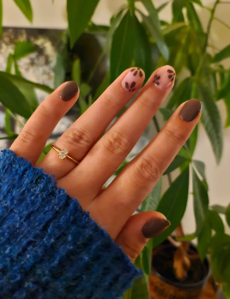 Hand with short espresso brown nails and two pink accent nails with brown petal print, wearing a blue knit sweater